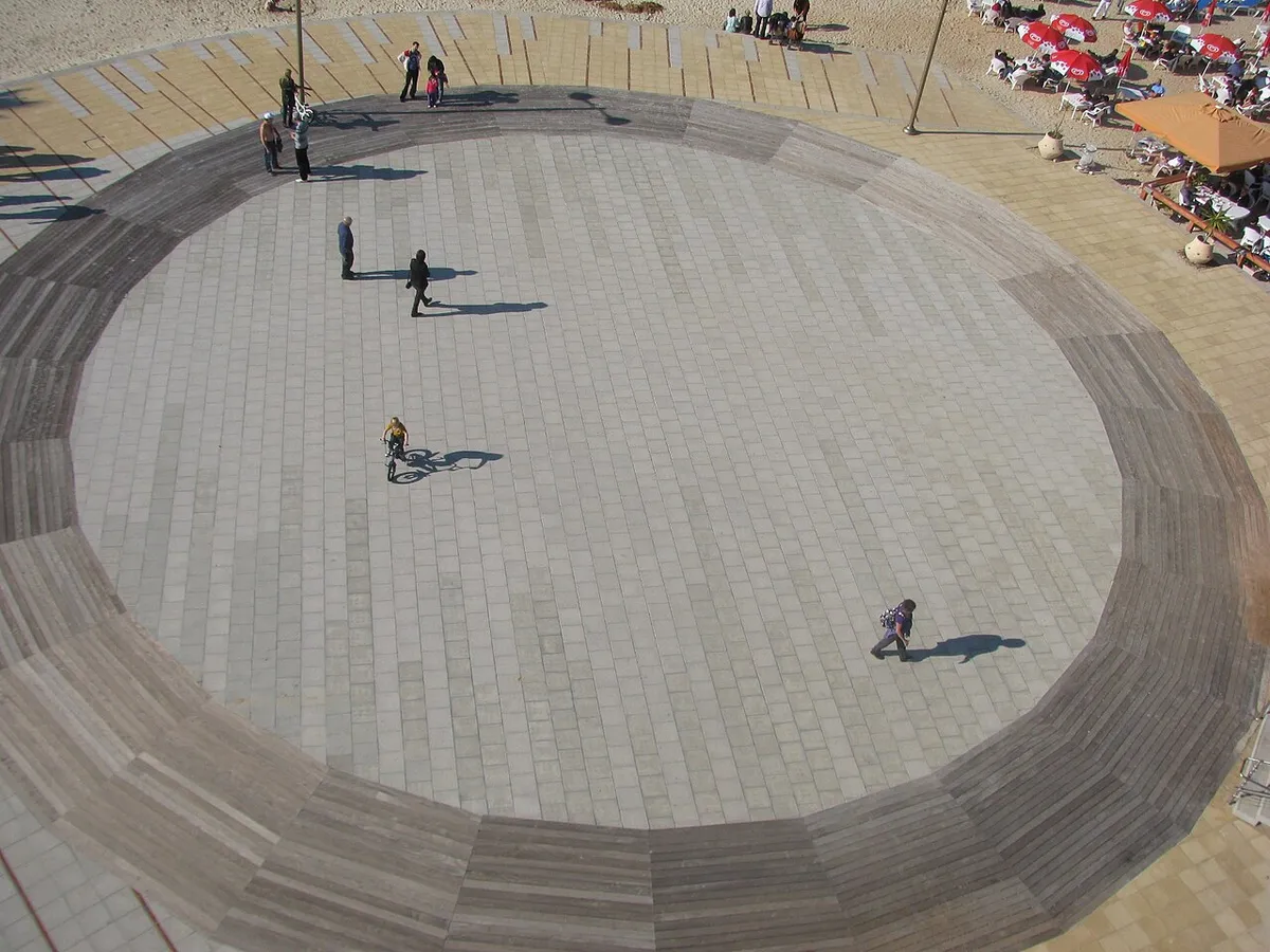 A round paved plaza on the Herzliya beach promenade seen from above, next to a beach cafe